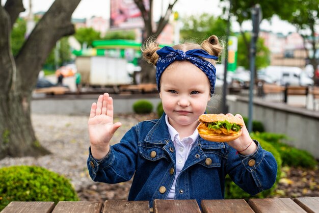 Cute little girl pointed stop gesture with burger in hands before eat in outdoors cafe