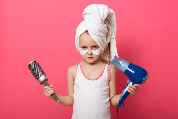 Cute little girl posing with round brush dryer and hairdryer in hands