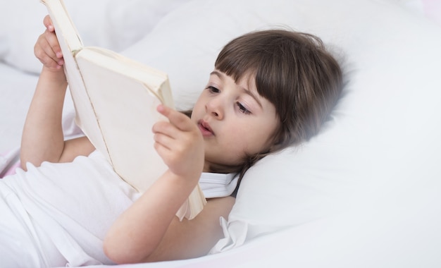 Cute little girl smiling while lying in a cozy white bed with , the concept of children's rest and sleep