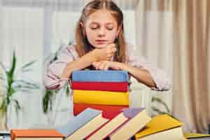 Free photo cute little girl at the table with a lot of colorful books.