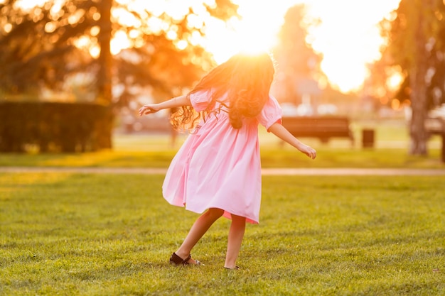 Cute little girl walking on grass at sunset