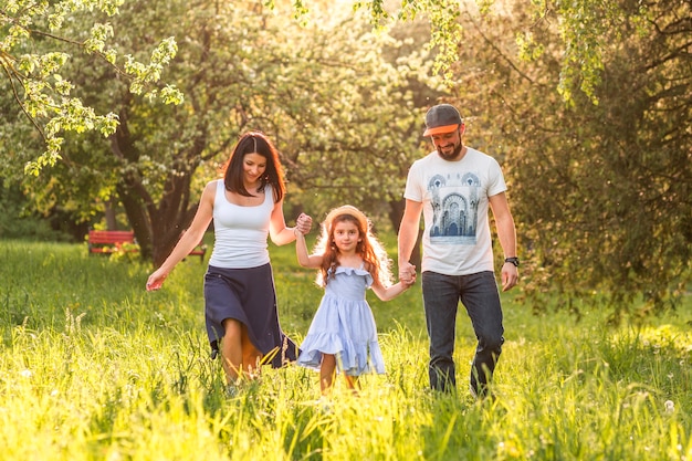 Cute little girl walking in park holding her parents hands