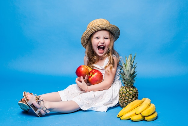 Free photo cute little girl with fruits isolated on a blue wall