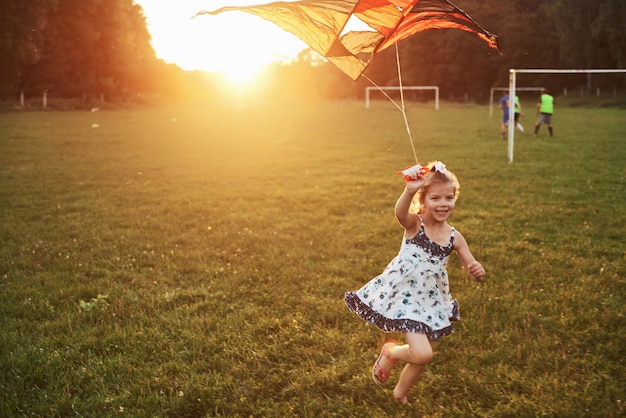 Free photo cute little girl with long hair running with kite in the field on summer sunny day