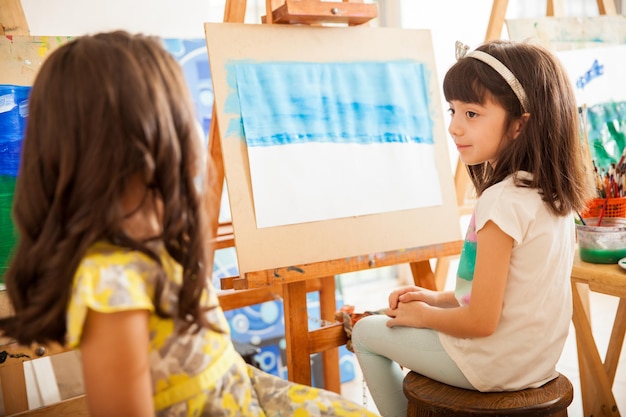 Cute little girls comparing each other's work and sharing ideas for her art class at school