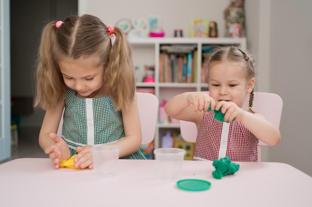 Cute little girls moulding from plasticine on pink table