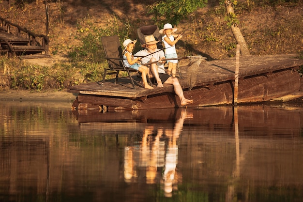 Free photo cute little girls and their granddad are on fishing at the lake or river