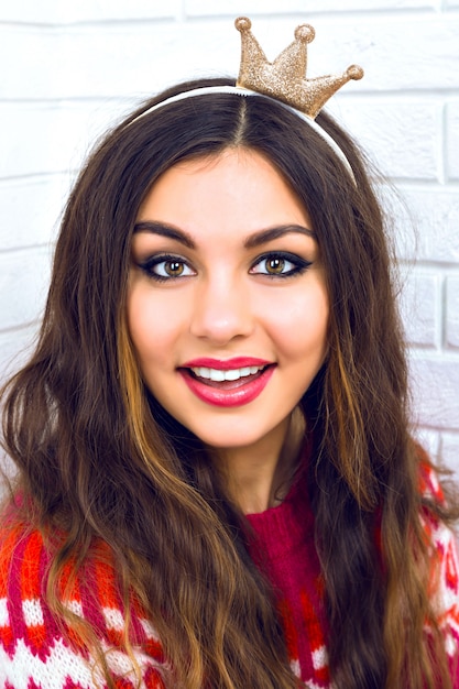 Cute outdoor portrait of pretty brunette woman wearing funny fake crown ready for party holidays time, wearing trendy cozy bright hipster sweater.