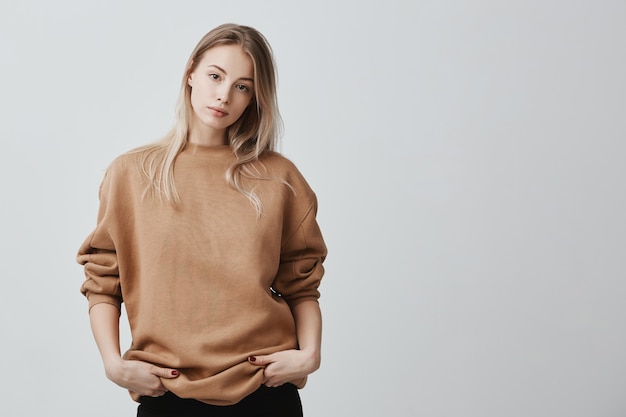 Free photo cute pretty beautiful woman wears loose sweater and black trousers, holds her hands in pocket