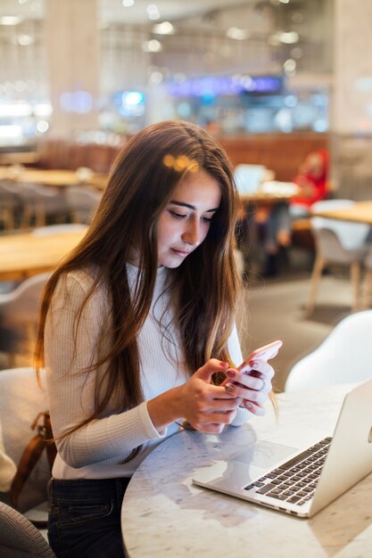 Cute and pretty young woman on smartphone in cafe