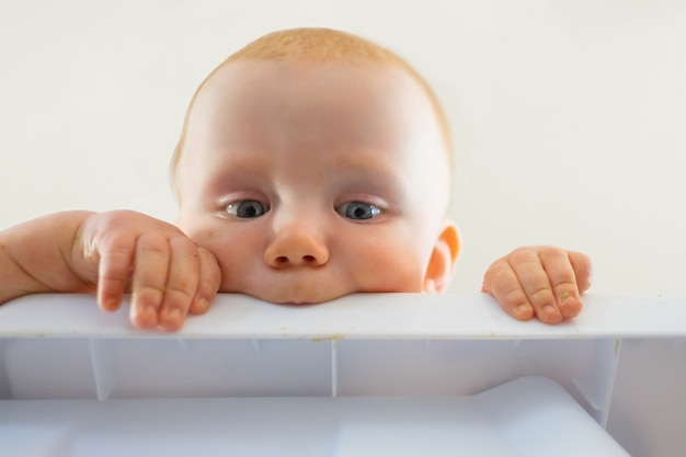 Cute red-haired hungry baby biting plastic board. Closeup view of curious newborn looking from table and holding it. Childhood and infancy concept