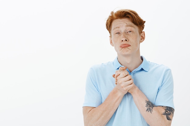 Free photo cute redhead man clench hands in plead, begging for help, need something, looking silly