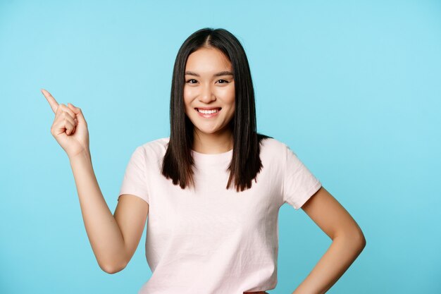 Cute smiling asian brunette student pointing at upper left corner showing company name promo banner ...