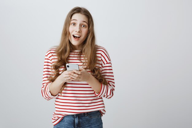 Cute smiling girl holding smartphone and looking pleased