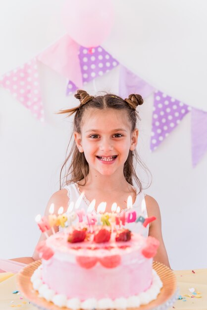 Cute smiling little girl standing near birthday cake