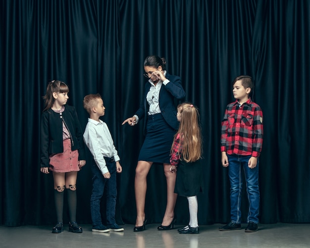 Free photo cute stylish children on dark studio background. the beautiful teen girls and boy standing together