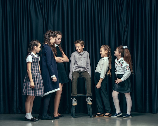 Free photo cute stylish children on dark studio. the beautiful teen girls and boy standing together