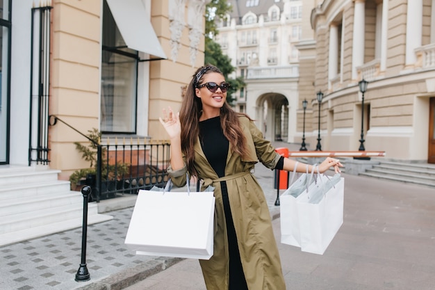 Free photo cute tanned woman in elegant sunglasses walking down the street with packages from store