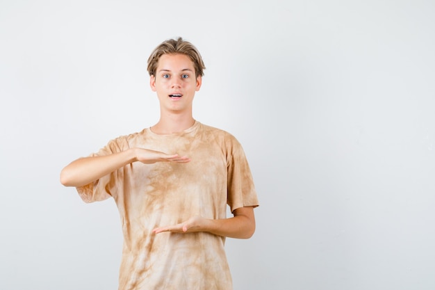 Free Photo cute teen boy showing size sign in t-shirt and looking wondered , front view.