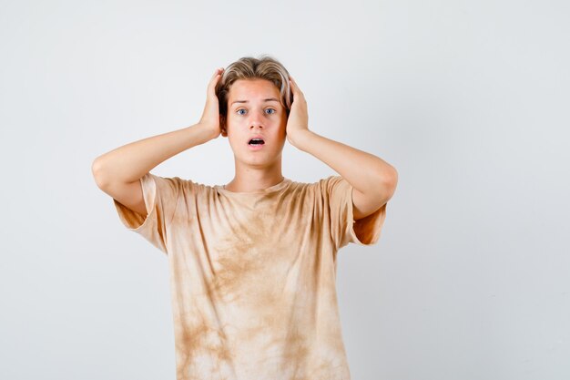 Cute teen boy in t-shirt keeping hands on head and looking anxious , front view.