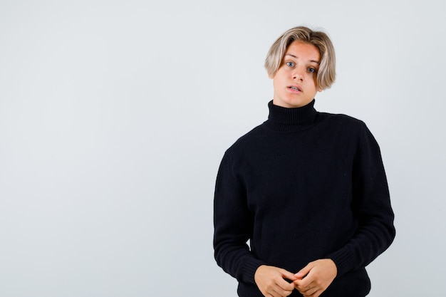 Cute teen boy in turtleneck sweater looking at camera and looking bewildered