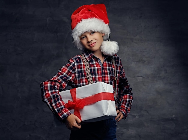 Free Photo cute teenage boy in santas' hat dressed in a plaid shirt holds big present gift box.