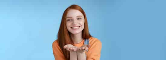 Free photo cute tender kind young ginger girl giving all love you hold something palms showing camera smiling delighted introduce present grinning romantic gesture send air kisses blue background