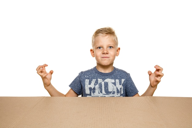 Free Photo cute and upset little boy opening the biggest postal package. disappointed young male model on top of cardboard box looking inside.