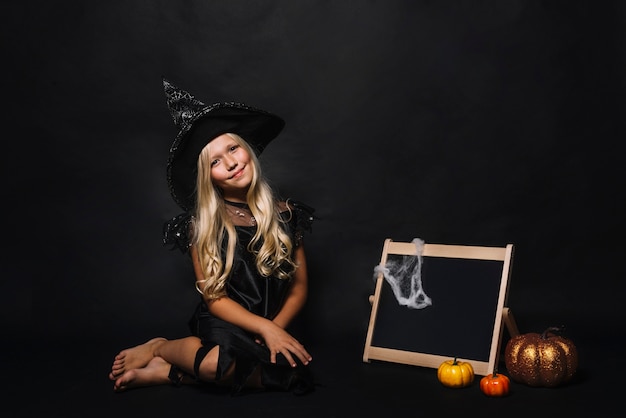 Free Photo cute witch near blackboard and pumpkins