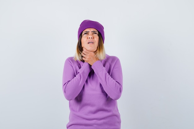 Cute woman suffering from sore throat in sweater, beanie and looking sick . front view.