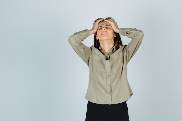 Free photo cute young female clasping head with hands in shirt, skirt and looking mournful , front view.