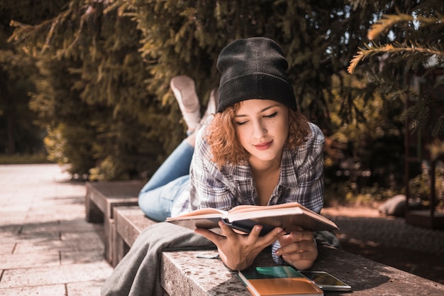 Free photo cute young female in hat reading book in park