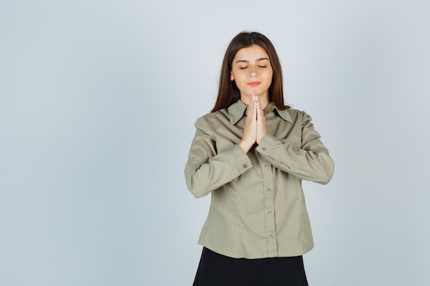 Free photo cute young female showing namaste gesture in shirt, skirt and looking hopeful , front view.