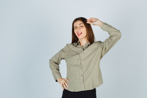 Cute young female showing salute gesture while winking in shirt and looking confident. front view.