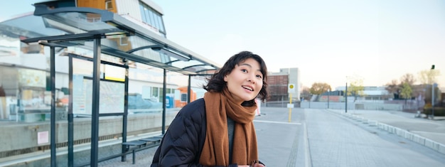 Cute young girl student waiting on a bus stop looking for her public transport on app tracker