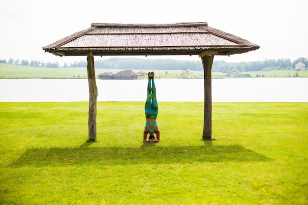 Cute young woman doing handstand exercises in the green park