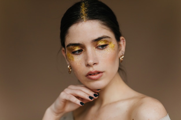 Free Photo cute young woman with sparkle makeup posing on brown wall.  close-up shot of debonair black-haired female model.