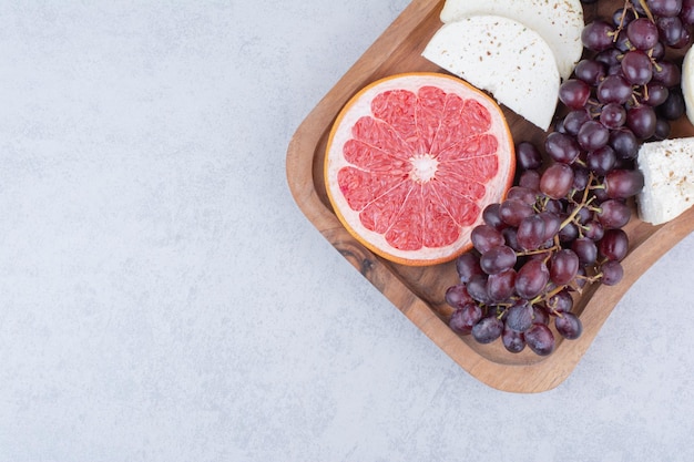 A cutting board full of cheese, slice of grapefruit and grapes. High quality photo