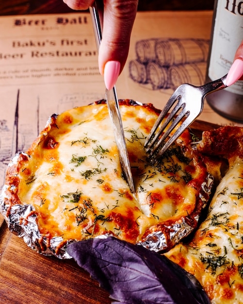 Free photo cutting food with melted cheese and herbs with cutlery.