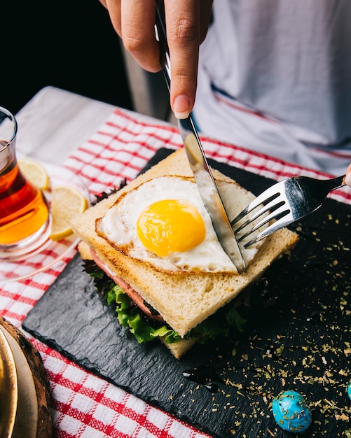 Free photo cutting sandwich with fried egg with knife and fork.