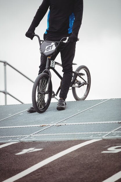 Cyclist standing with BMX bike at starting ramp