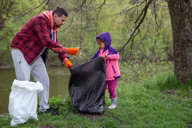 Dad and daughter, with garbage bags, clean the environment of garbage.