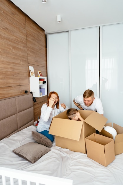 Dad, mom and little son play in the bedroom with paper boxes