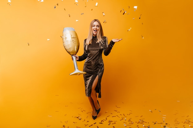 Free photo dancing appealing woman posing on orange under cinfetti. indoor portrait of glamorous caucasian woman with wineglass expressing sincere emotiins.