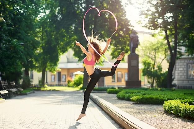 Dancing girl making pirouettes with a ribbon in the city park.