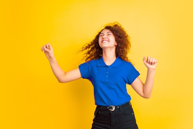 Dancing with flying hair. Caucasian teen's girl portrait on yellow studio background. Beautiful female curly model. Concept of human emotions, facial expression, sales, ad, education. Copyspace.