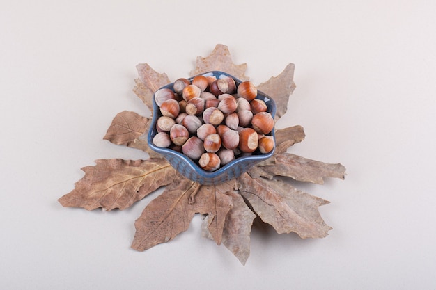 Dark bowl of shelled natural hazelnuts and dry leaves on white background. High quality photo