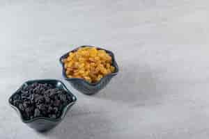 Free photo dark bowls with dried golden and black raisins on stone background.