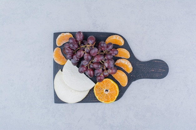 Free photo a dark cutting board with sliced cheese and fruits.