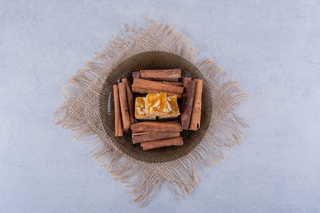 Dark glass bowl of cinnamon sticks and nut candies on stone table. 